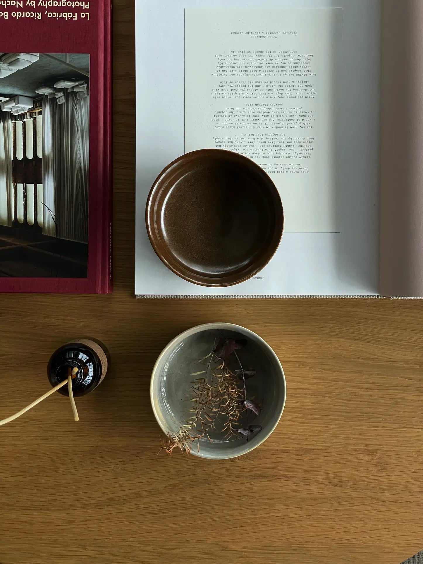 A tabletop displays an open book and the ves Aki Bowl, Set of 2 by ves, alongside a ceramic bowl with dried leaves and a small incense holder—all neatly arranged to showcase East Asian tableware.