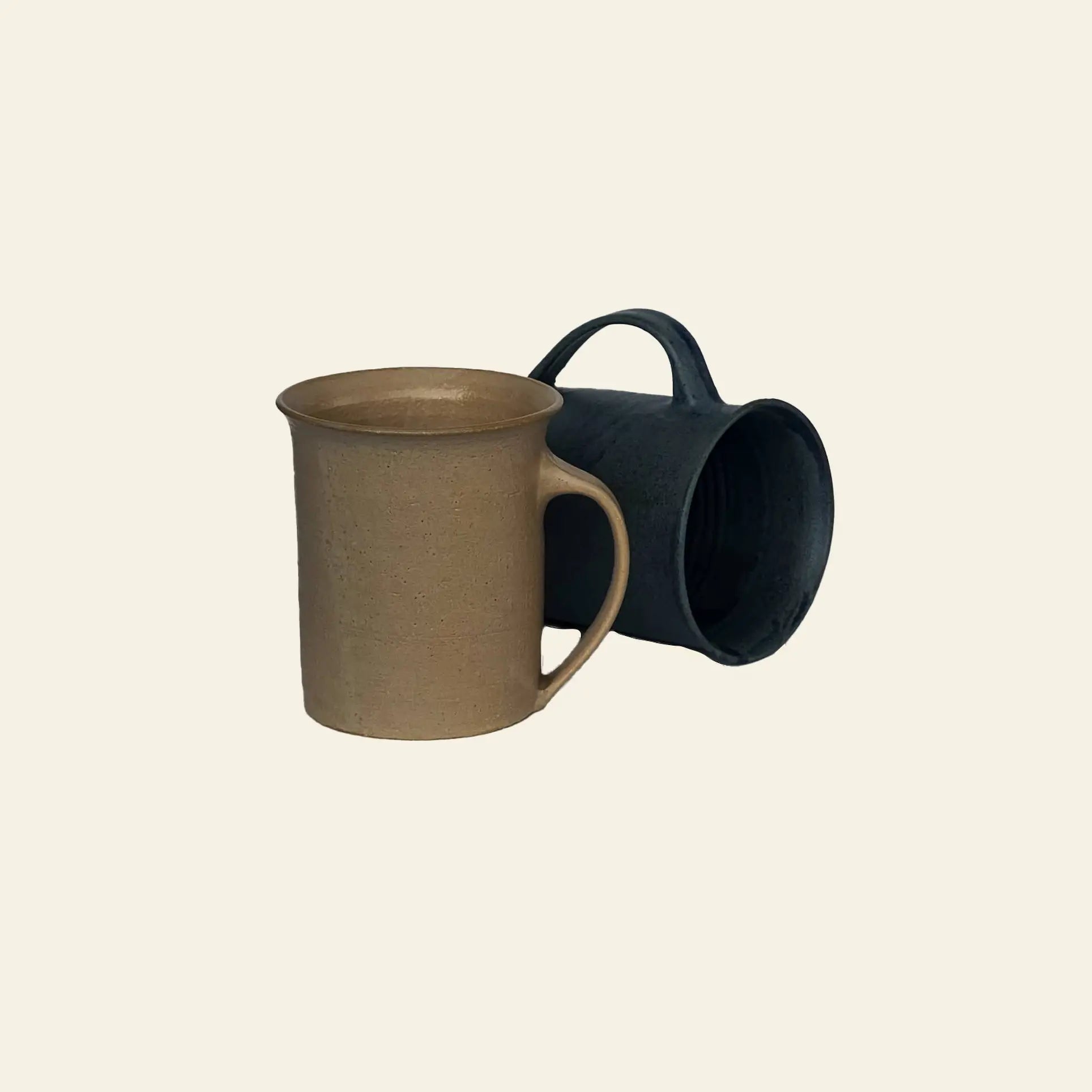 The ves Kura Mug, Set of 2 by ves features one upright beige mug and one dark blue mug on its side, both with ergonomic handles, displayed against a plain light background.
