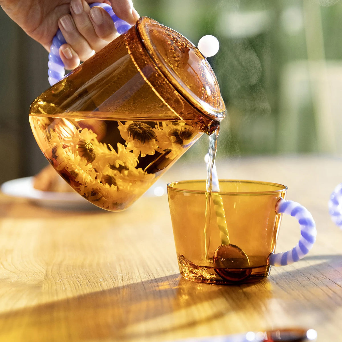 Chrysanthemum tea pouring from an amber glass teapot into a matching glass
