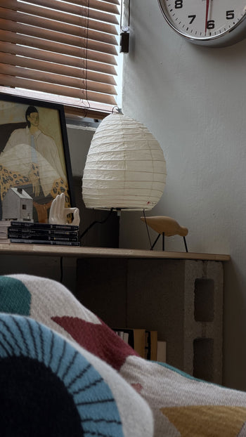 The Akari 1N by Akari is a white, oval paper lantern lamp with slim metal legs and a black power cord, glowing gently against a plain background—a modern design inspired by Akari Light Sculptures.