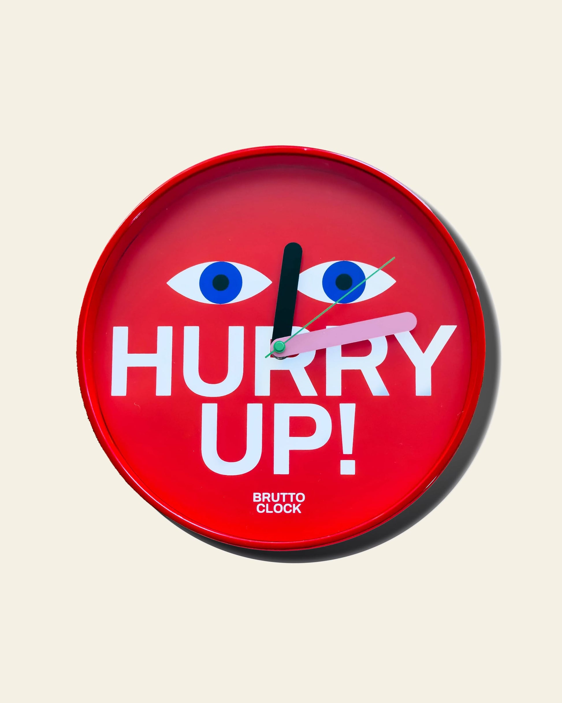 The Brutto Studio Hurry Up! Wall Clock features multicolour design with blue cartoon eyes, bold white "HURRY UP!" text, and "BRUTTO CLOCK" below. Set at 2:08 on an off-white background, it offers silent quartz movement for quiet spaces.