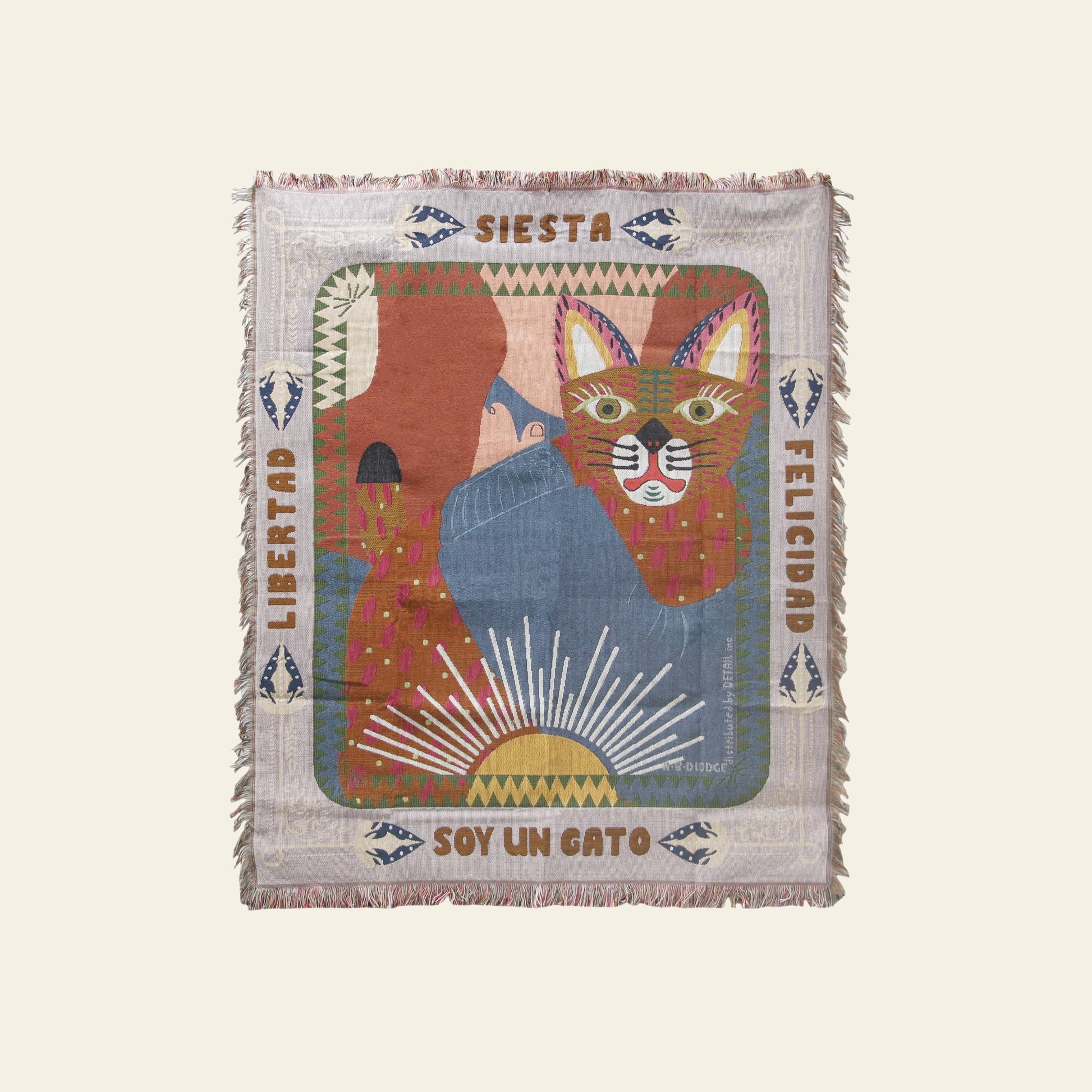 The DETAIL Cat Oax Throwket by DETAIL is a colorful folk art blanket with a cat, sun rays, and abstract shapes. Spanish words like Libertad, Siesta, Felicidad, and Soy un gato border the fringed cat throw blanket.