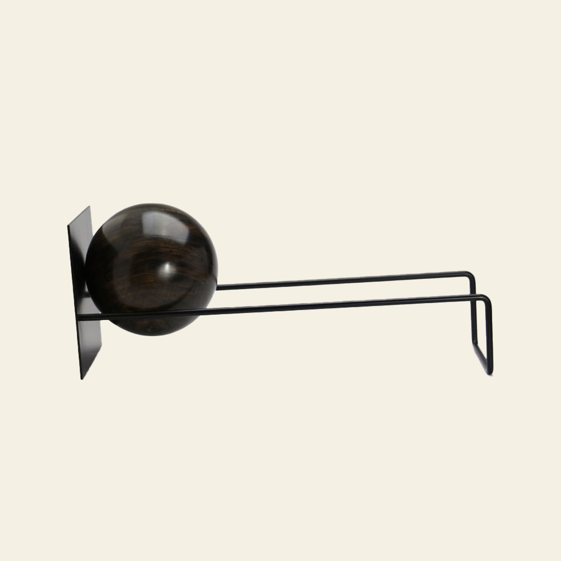 The DETAIL Slope Bookend by DETAIL features a minimalist black wall-mounted design with two parallel metal rods and a dark wooden sphere, creating a sculptural look reminiscent of modern art.