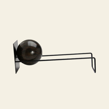The DETAIL Slope Bookend by DETAIL features a minimalist black wall-mounted design with two parallel metal rods and a dark wooden sphere, creating a sculptural look reminiscent of modern art.