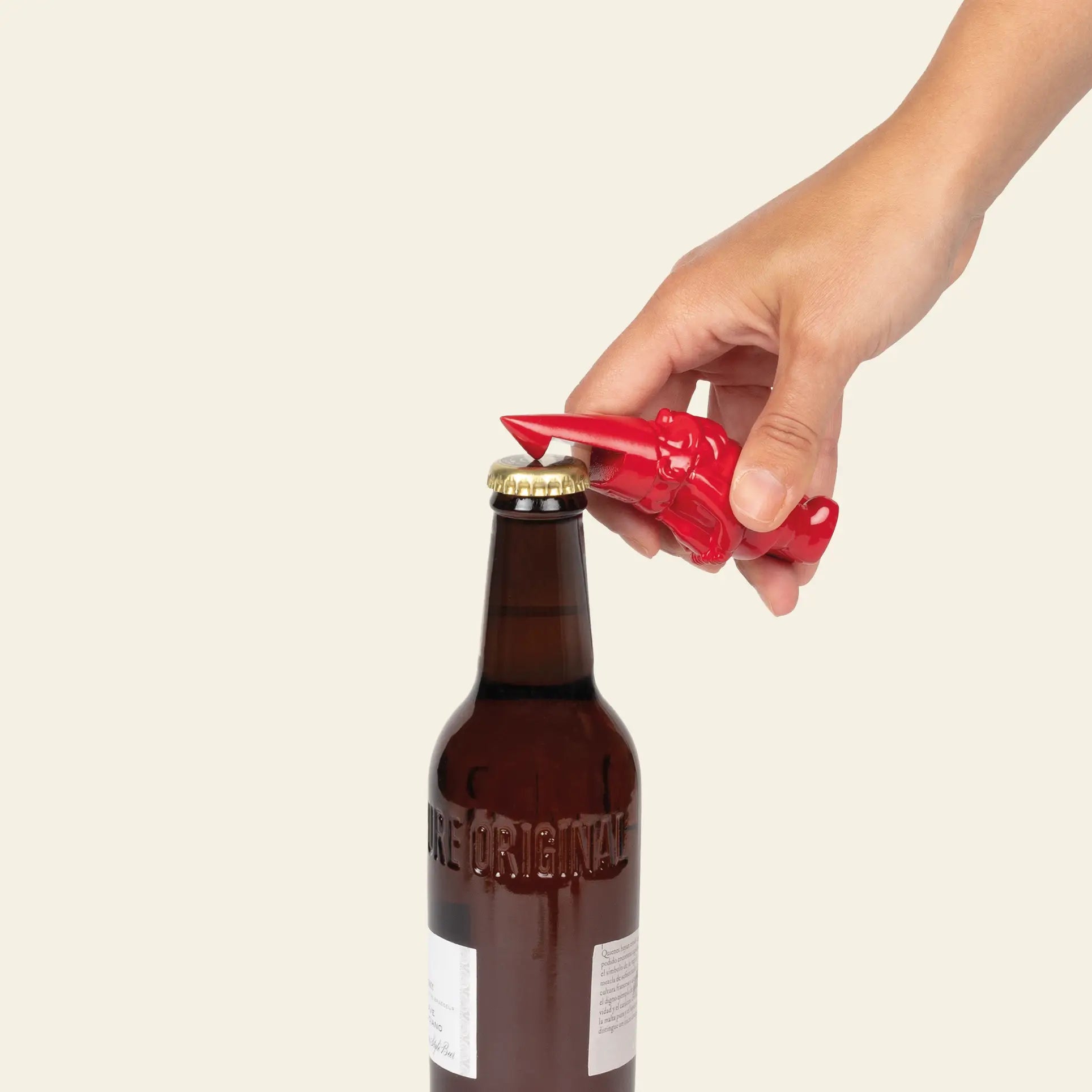 A hand uses the DOIY Gnome Bottle Opener by DOIY to open a brown glass bottle against a plain light background.