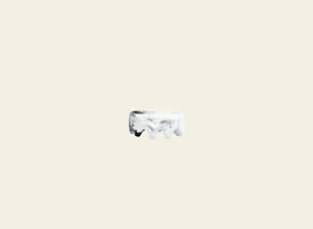 A small, round Dinosaur Designs Crown Dish sits centered on a plain light beige background, its sculptural white form echoing the iconic style of Dinosaur Designs.