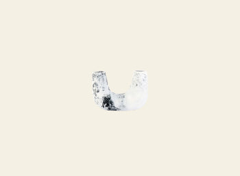A small, white, U-shaped Dinosaur Designs Mini Branch Vase with a rough texture and black speckles is centered on a plain beige background.