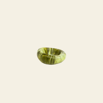The Dinosaur Designs Small Drift Dish is a round green glass bowl with a marbled pattern, offering an organic presence and presented elegantly on a plain off-white background.