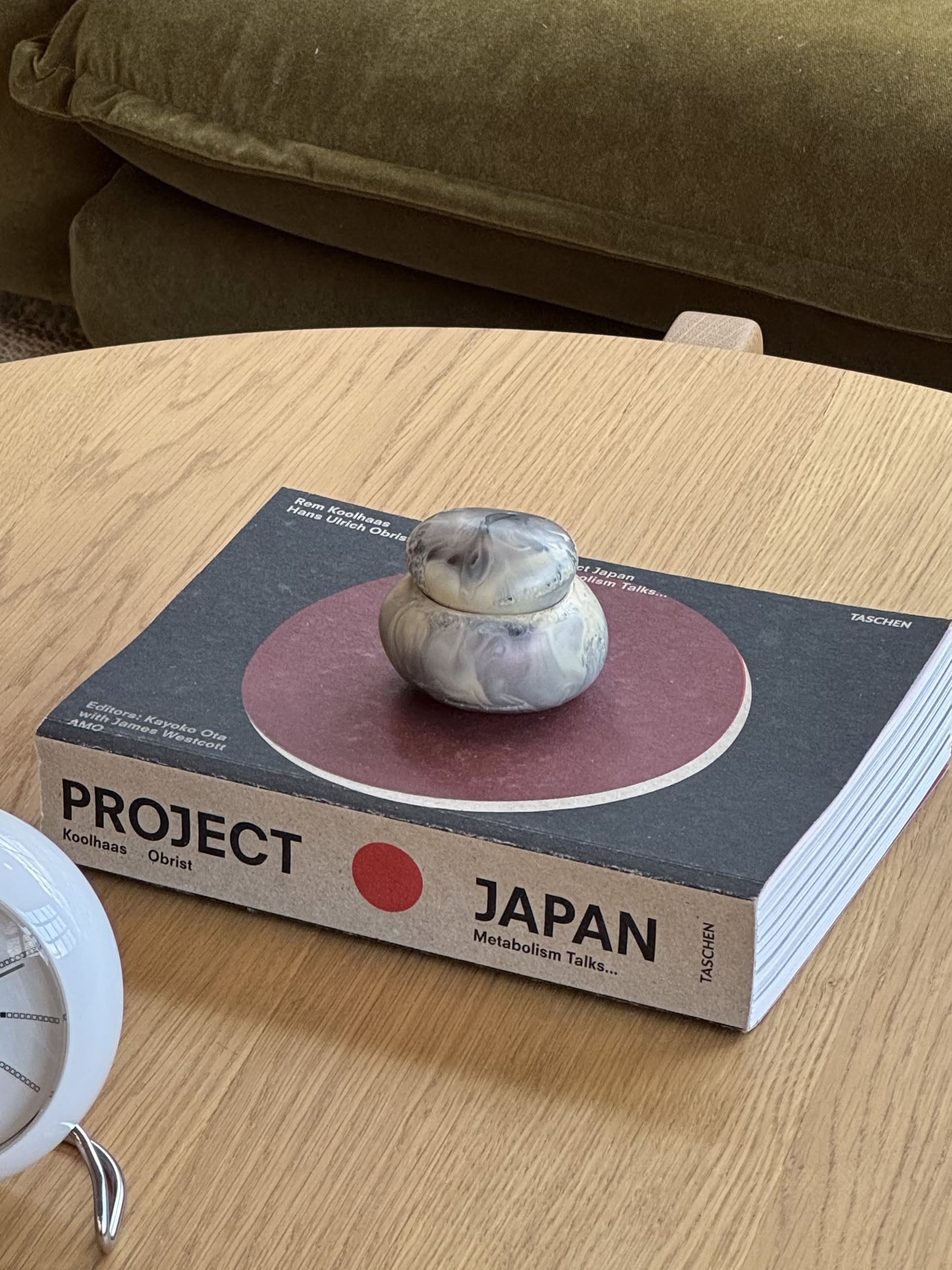 The Dinosaur Designs Small Pebble Jar, handmade from stone or ceramic with a sculptural design and matching lid, sits on a plain light beige background.