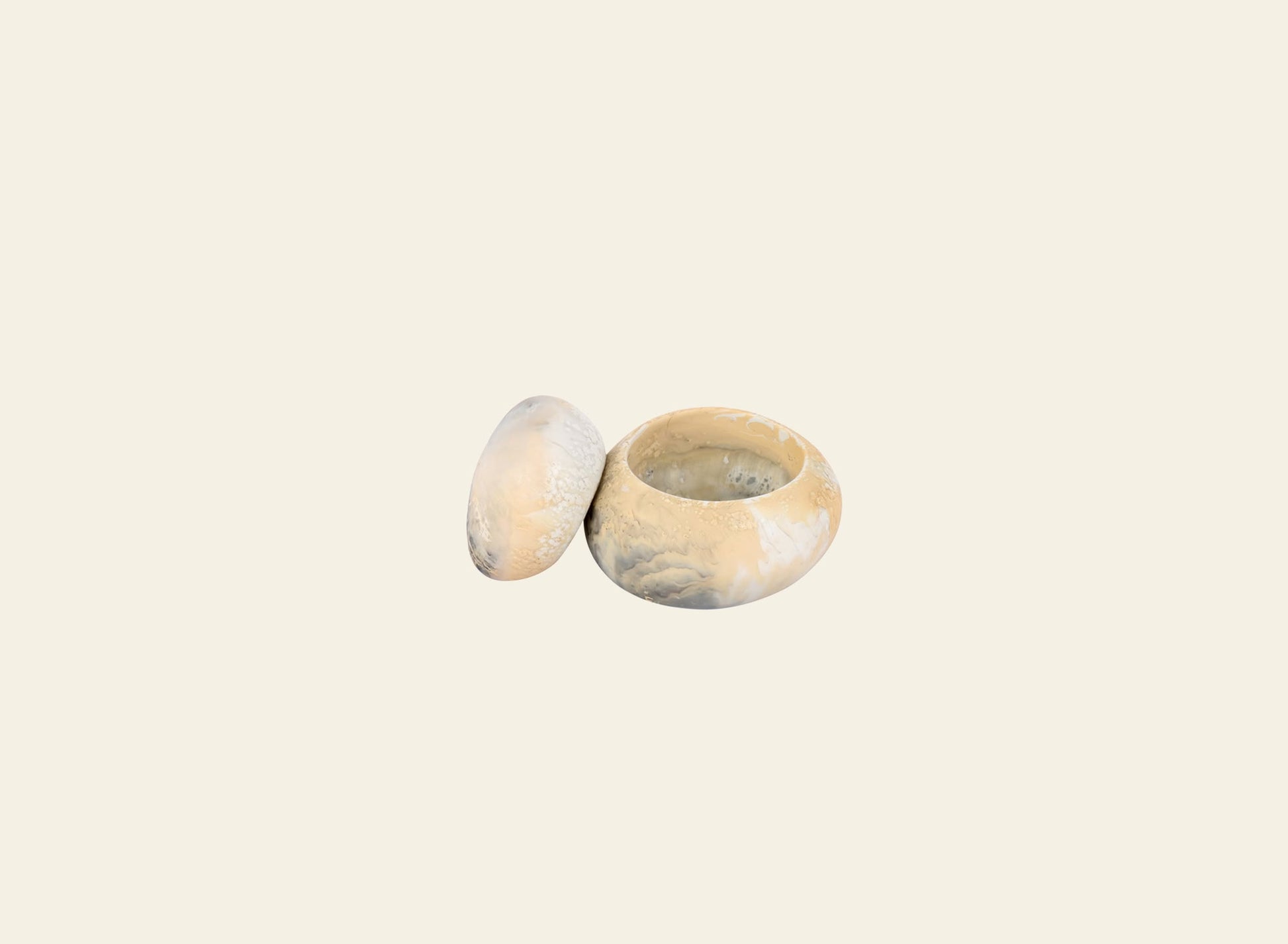 A Dinosaur Designs Small Pebble Jar with a sculptural, round form sits on a thick book titled PROJECT JAPAN atop a wooden table, with part of a green couch seen in the background.