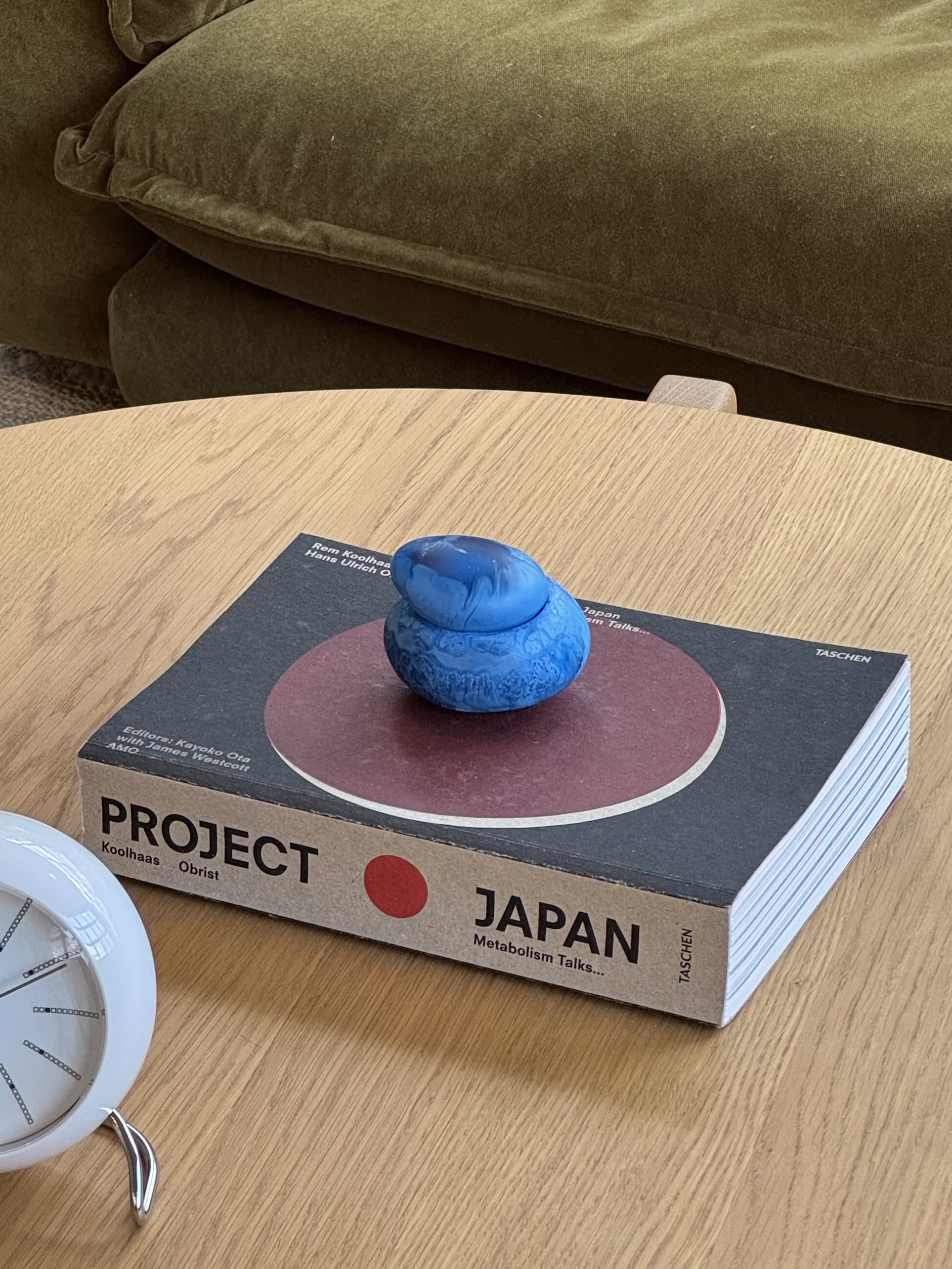 The Dinosaur Designs Small Pebble Jar by Dinosaur Designs is a small, round, blue jar with a matching lid beside it, both featuring a sculptural design set against a plain, light beige background.