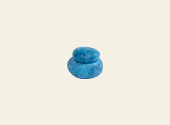 The Dinosaur Designs Small Pebble Jar by Dinosaur Designs is a blue, marbled, sculptural jar with a matching lid, shown against a plain light beige background.