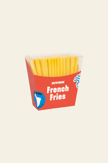 A hand holds an Eat My Socks French Fries Socks box from the brand Eat My Socks, filled with yellow socks. Other fun fashion socks by Eat My Socks, styled after quirky accessories and foods, are displayed on a wooden table.