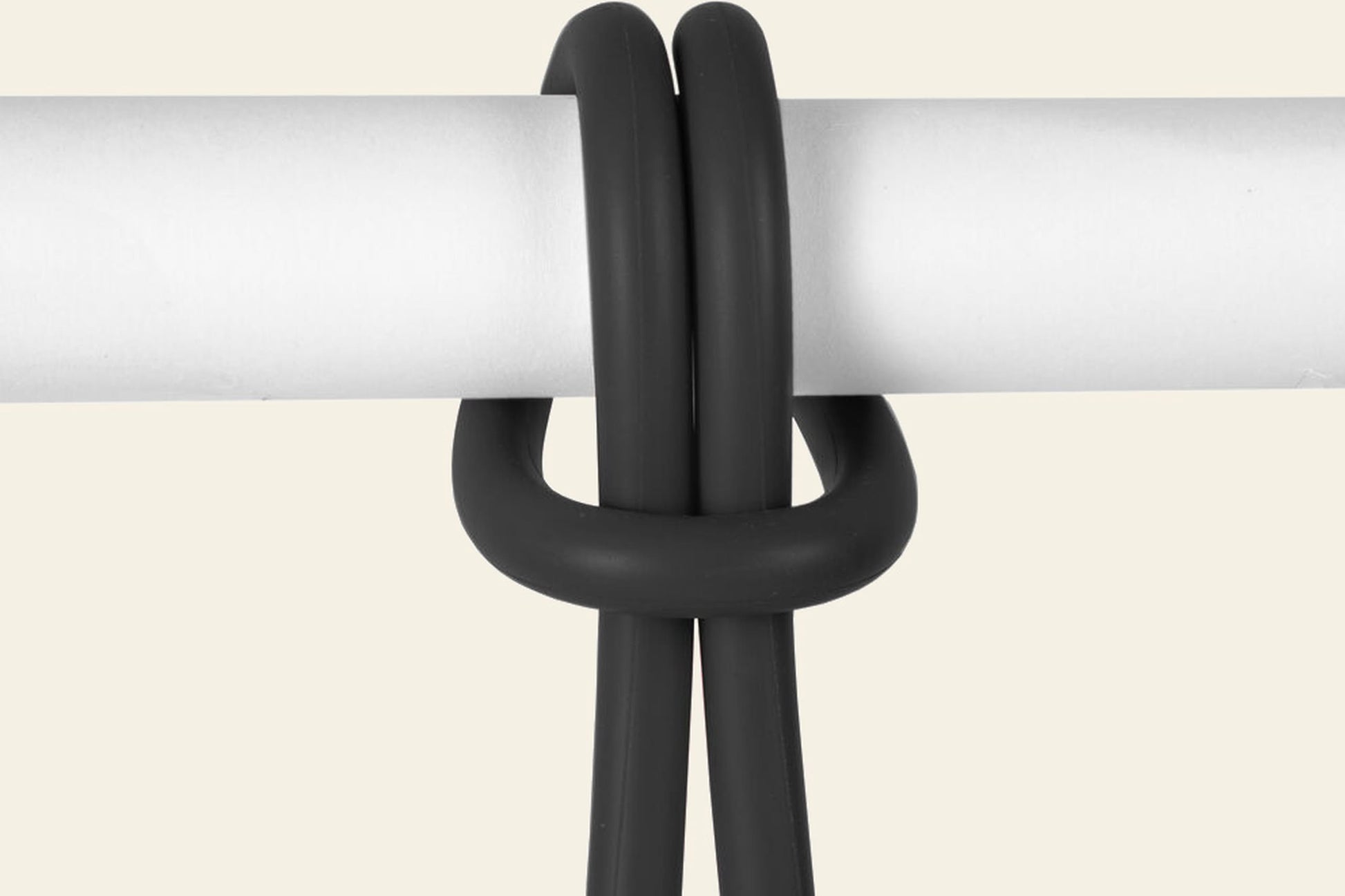 A black Fatboy Bolleke cable from Fatboy is looped over a horizontal white rod, forming a neat, symmetrical knot against a light beige background.