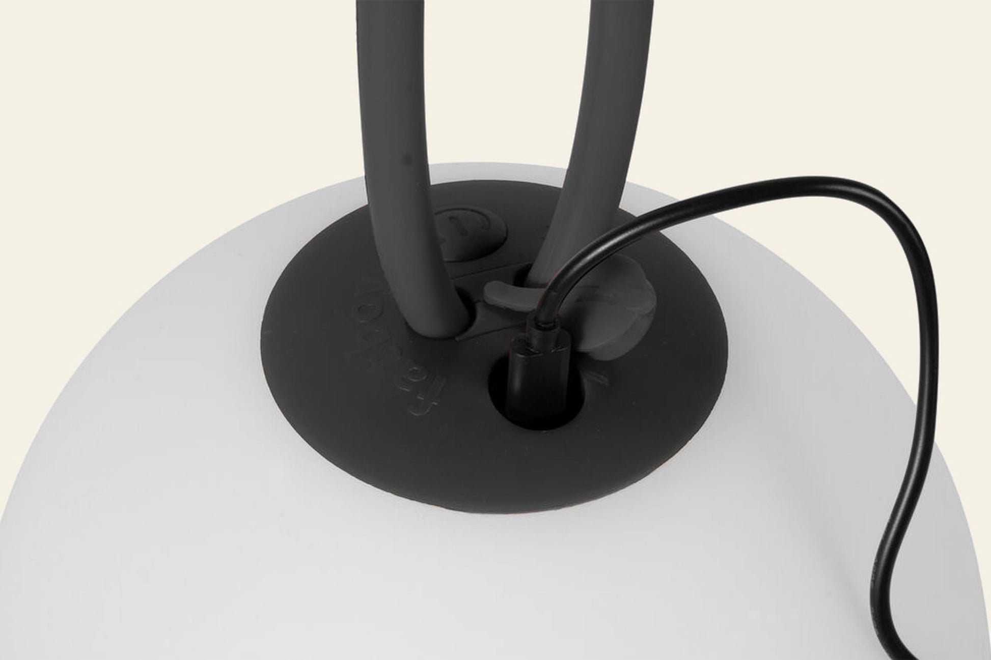Close-up of a black cable connected to the Fatboy Bolleke by Fatboy—a smooth, white portable light with two thick black handles. Ideal for outdoor use, it sits against a light beige background.