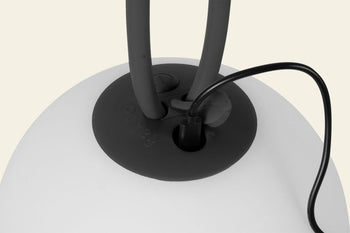 Close-up of a black cable connected to the Fatboy Bolleke by Fatboy—a smooth, white portable light with two thick black handles. Ideal for outdoor use, it sits against a light beige background.