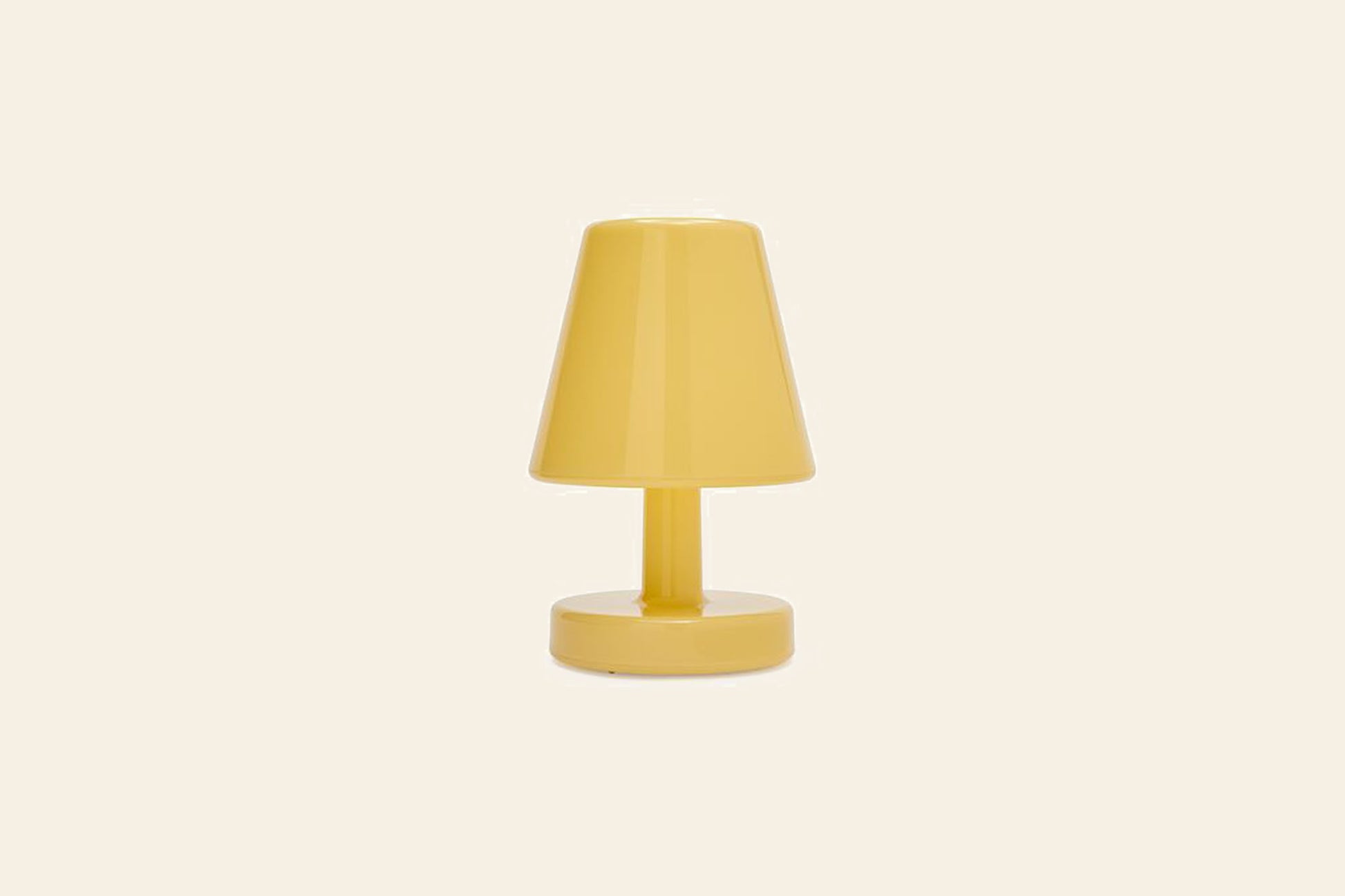 A compact, modern yellow Fatboy Edison The Ambiance LED wireless lamp with a round base and conical shade, set against a plain beige background. Inspired by Fatboy’s playful rechargeable table lamp design.