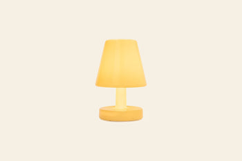 The Fatboy Edison The Ambiance by Fatboy is a modern yellow rechargeable table lamp with a conical shade and round base, illuminated and set against a plain light beige background.