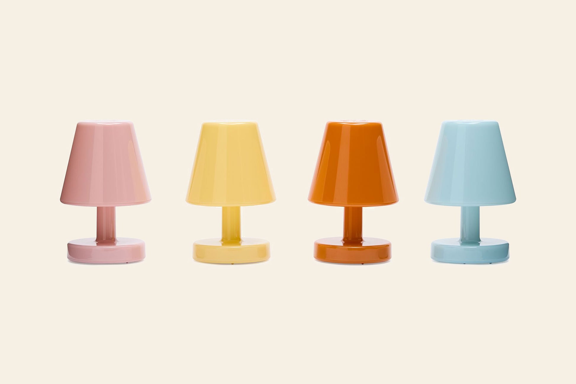 Four Fatboy Edison The Ambiance LED wireless lamps in pastel pink, yellow, orange, and light blue are lined up side by side against a neutral beige background.