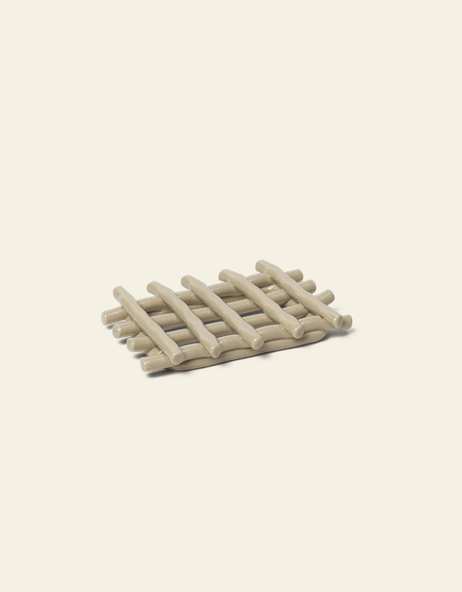 The Ferm Living Ceramic Soap Tray in Cashmere is a rectangular trivet with a woven lattice design, ideal as a handmade soap dish or bathroom accessory, shown against an off-white background.