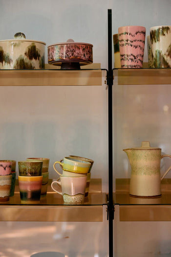HKliving 70s Ceramics: Americano Mugs, Set of 4 by HKliving showcases pastel hues and retro patterns, displayed on gold metal shelves with a light backdrop.