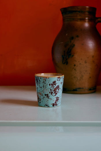 The HKliving 70s Ceramics: Coffee Mugs, Set of 6, is featured on a light surface in front of a large rustic brown jug with an orange wall background.