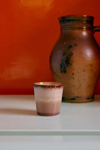 The HKliving 70s Ceramics Coffee Mugs Set of 6 features small ceramic mugs with a brown gradient glaze, evoking retro style as they sit on a light surface before a rustic jug and orange backdrop.