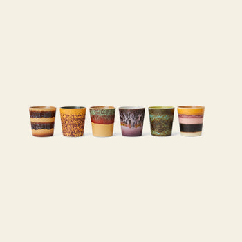 The HKliving 70s Ceramics: Coffee Mugs, Set of 6 features uniquely patterned mugs in earthy tones—brown, yellow, orange, and green—each with a distinct 70s-inspired design. Arranged in a row against a plain light background.