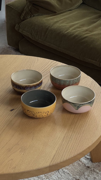 The HKliving 70s Ceramics Dessert Bowls, Set of 4, in vibrant retro colors are displayed on a round wooden coffee table with a green sofa in the background.