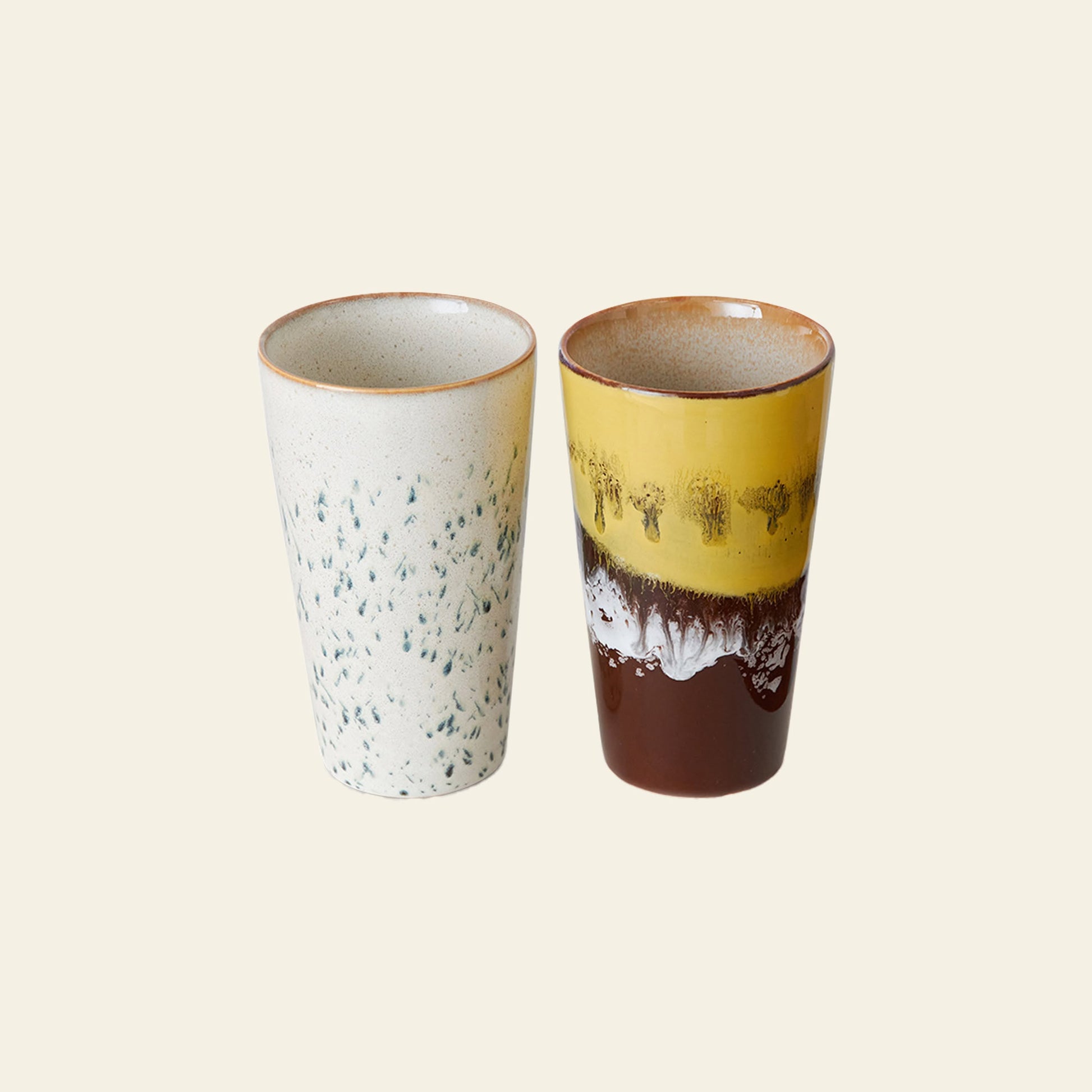 The HKliving 70s Ceramics: Latte Mugs, Set of 2 features one off-white mug with blue speckles and another with a brown base, white middle, and mustard yellow top—perfect for enjoying your morning latte in style.