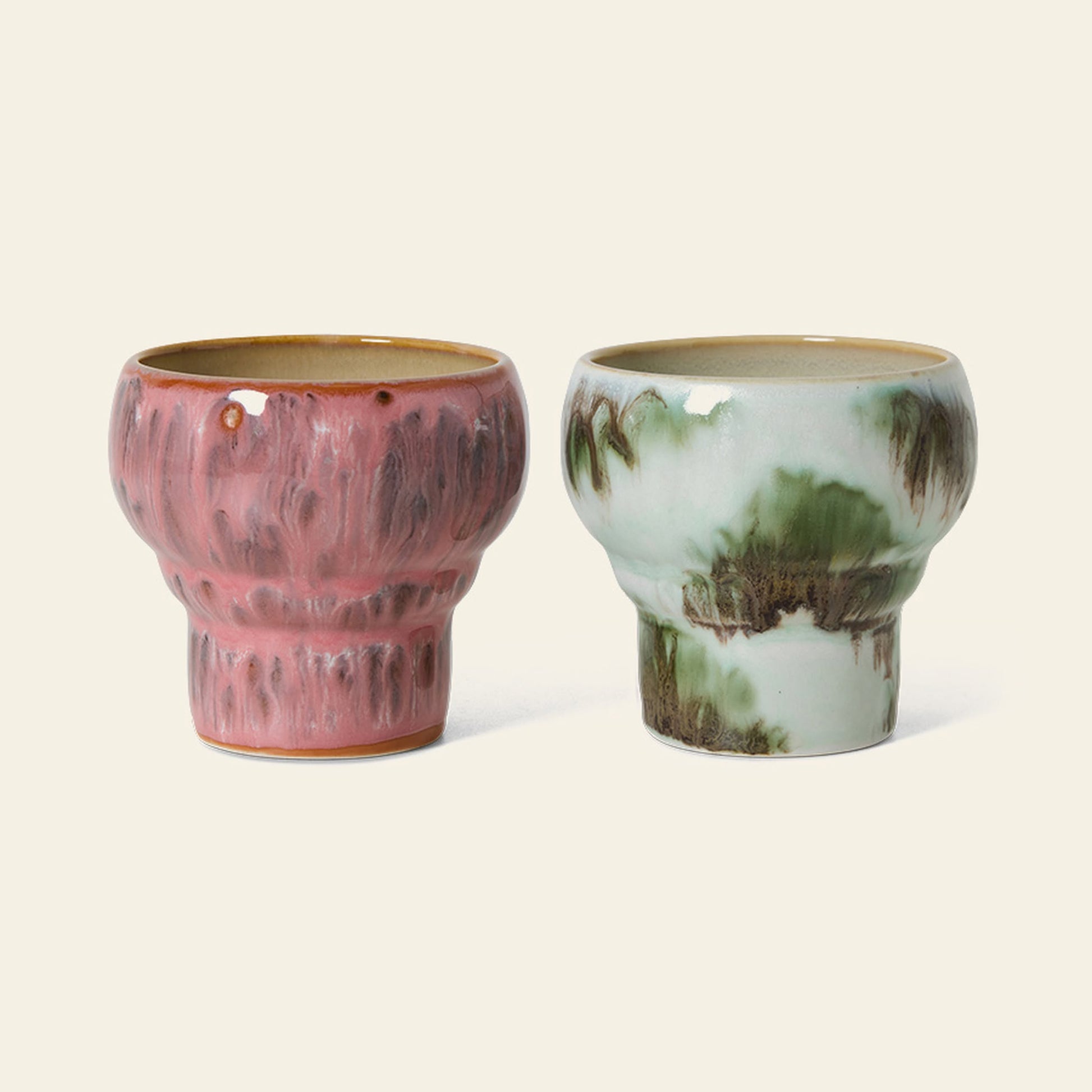 The HKliving 70s Ceramics: Lungo Mugs, Set of 2 features handcrafted stoneware mugs with rounded shapes—one in pink and brown glaze, the other in green and brown—reflecting artistic '70s-inspired style.