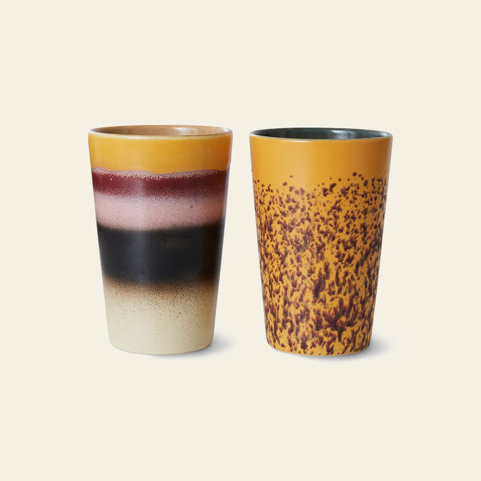 The HKliving 70s Ceramics: Tea Mugs, Set of 2 features one mug with layered cream, black, burgundy, and mustard yellow bands, and another in mustard yellow with a brown speckled pattern—classic 70s style by HKliving.