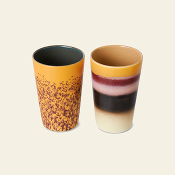 The HKliving 70s Ceramics: Tea Mugs, Set of 2 features one orange mug with brown speckles and one cream mug with yellow, brown, burgundy, and black bands—a charming retro set by HKliving inspired by classic 70s design.