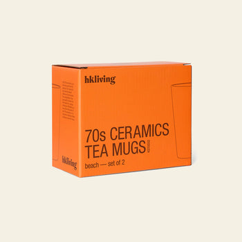 An orange box labeled “HKliving 70s Ceramics: Tea Mugs, Set of 2” rests on a light beige background. Simple mug sketches accentuate this stylish retro set from HKliving’s popular 70s Ceramics collection.