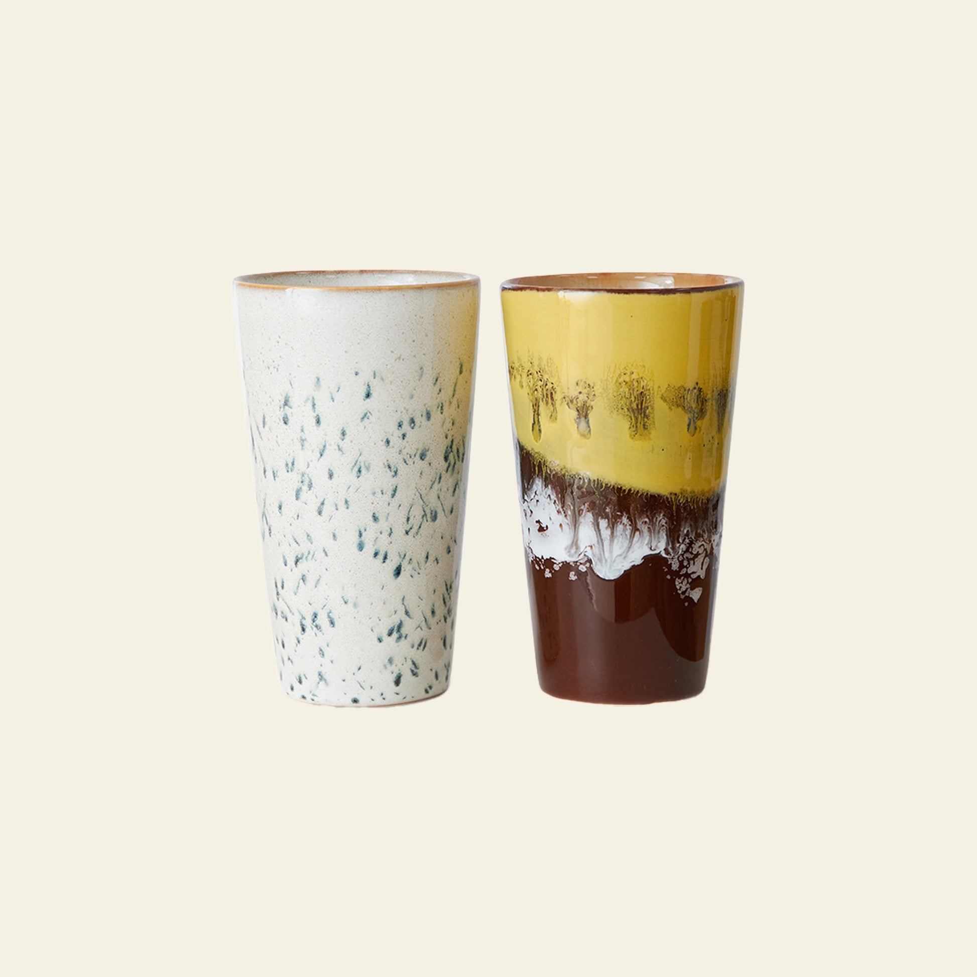 The HKliving 70s Ceramics: Latte Mugs, Set of 2, feature unique glazes—one white with blue speckles, the other brown with a yellow top—making them perfect for morning espresso and stylish on any neutral background.