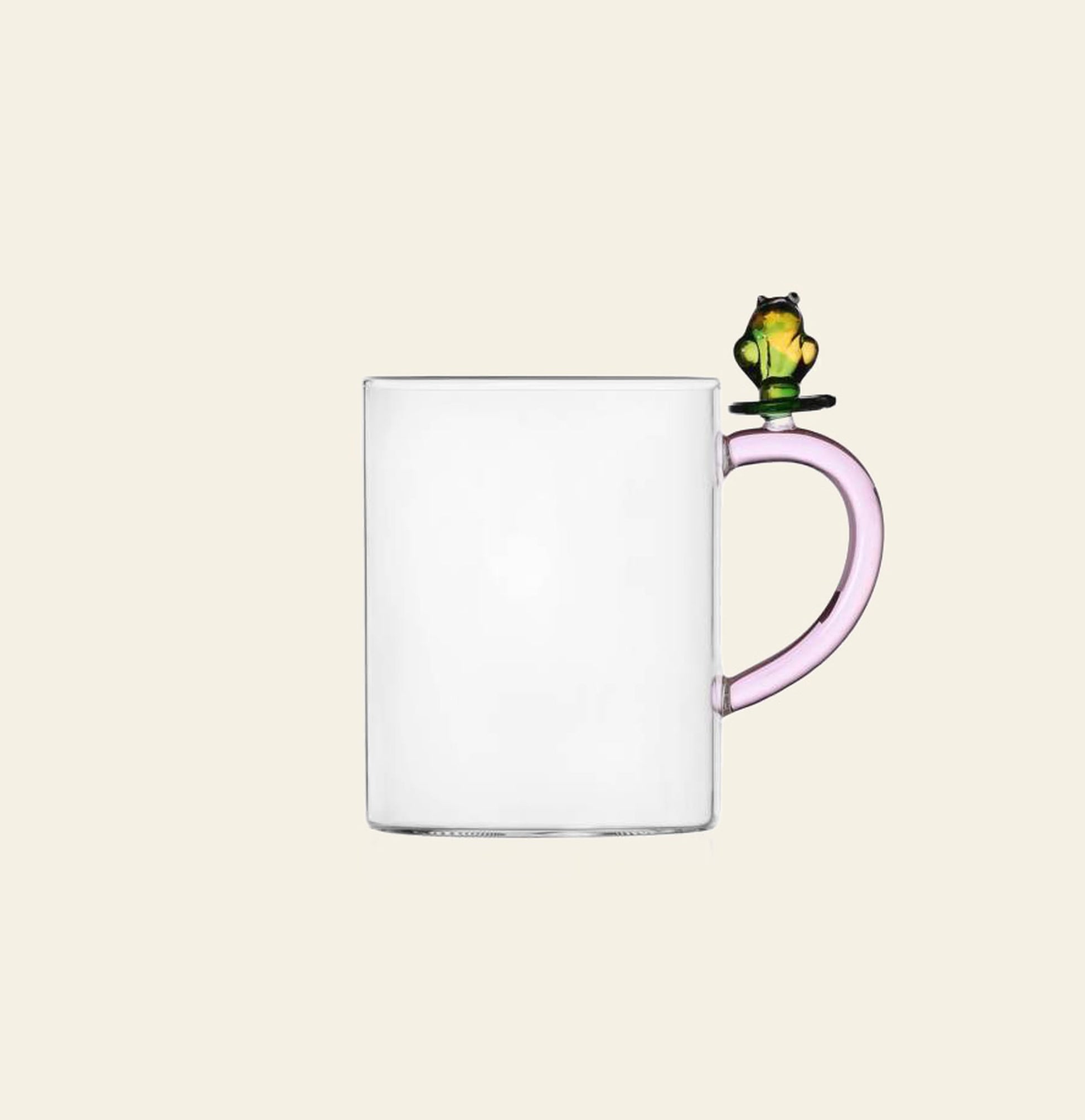 The Ichendorf Milano Fruits and Flower Mug is a clear glass mug with a light pink handle, adorned by a small green and yellow frog figurine designed by Alessandra Baldereschi for Ichendorf Milano.