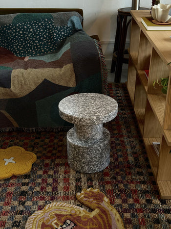 A Normann Copenhagen Bit Stool with a wide, circular seat in a speckled grey and white pattern, standing on a patterned rug.