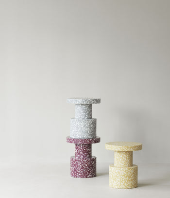 A stack of two speckled gray and dark red Normann Copenhagen Bit Stools next to a single yellow speckled sculptural stool.