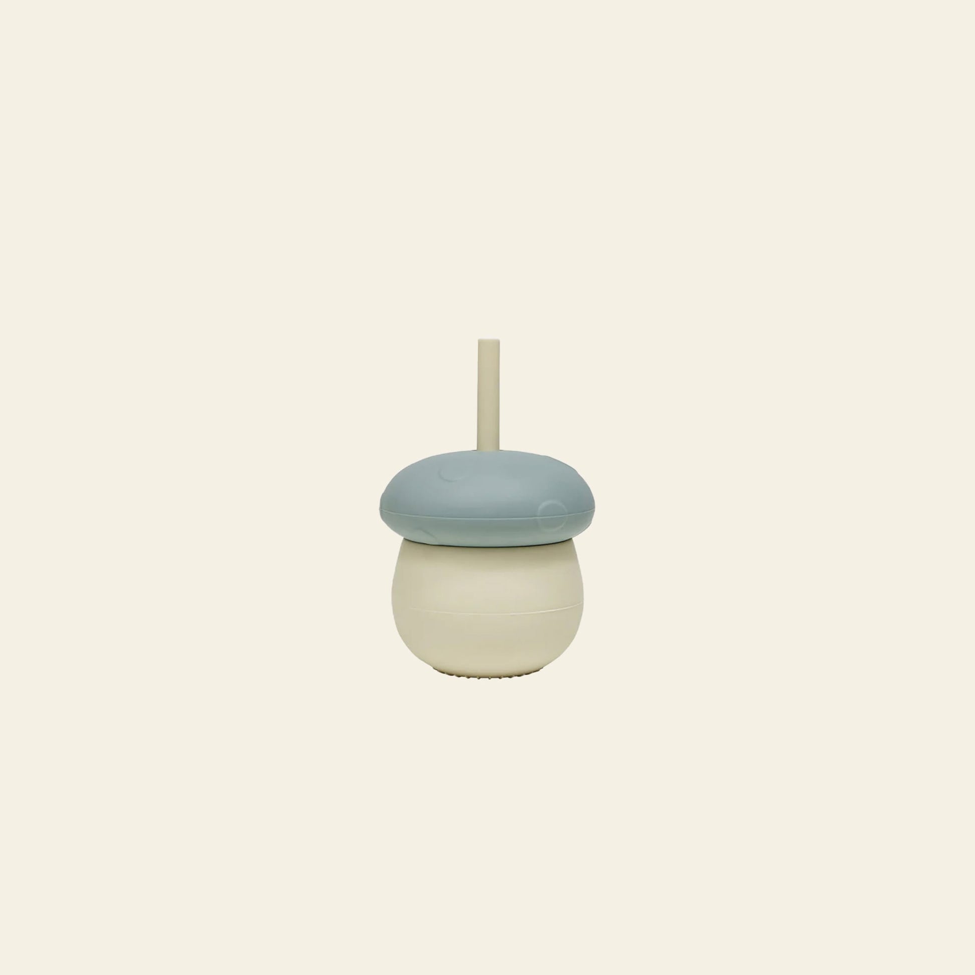 The OYOY Living Design Mushroom Cup by OYOY Living Design is a playful silicone cup with a blue lid and built-in straw, shaped like a mushroom, shown against a plain beige background.