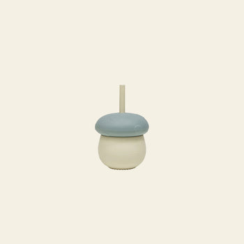 The OYOY Living Design Mushroom Cup by OYOY Living Design is a playful silicone cup with a blue lid and built-in straw, shaped like a mushroom, shown against a plain beige background.