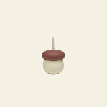The OYOY Living Design Mushroom Cup by OYOY Living Design features a playful beige base, a brown dome lid resembling an acorn cap, and a beige straw—an adorable silicone cup displayed on a plain off-white background.