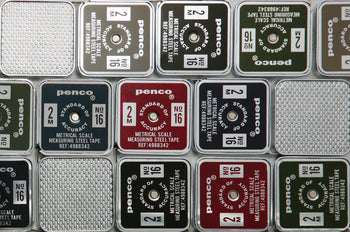A close-up of neatly arranged Penco Pocket Measure tapes in compact metal cases—silver, green, red, and black—each labeled with measurement details and model info.
