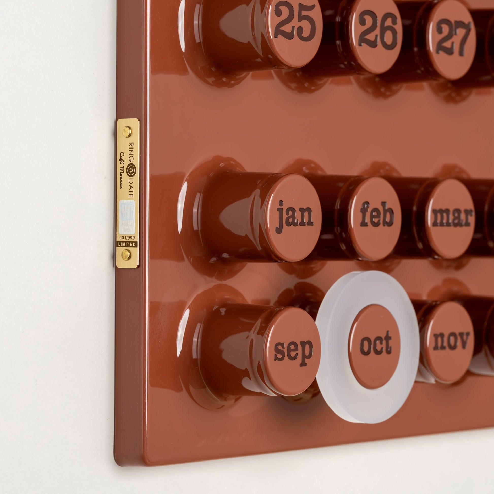 A close-up of the Ring-A-Date Limited Edition Wall Calendar - Cafè Mousse shows large round buttons for each date, a white ring on October, raised text, and a gold label. This vintage-style calendar is made by Ring-A-Date.