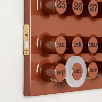 A close-up of the Ring-A-Date Limited Edition Wall Calendar - Cafè Mousse shows large round buttons for each date, a white ring on October, raised text, and a gold label. This vintage-style calendar is made by Ring-A-Date.