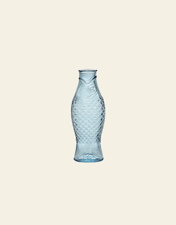 The Serax Fish & Fish Carafe by Serax features detailed scales and fins in clear blue glass, standing upright for a striking look—an eye-catching piece to enhance your tableware collection.