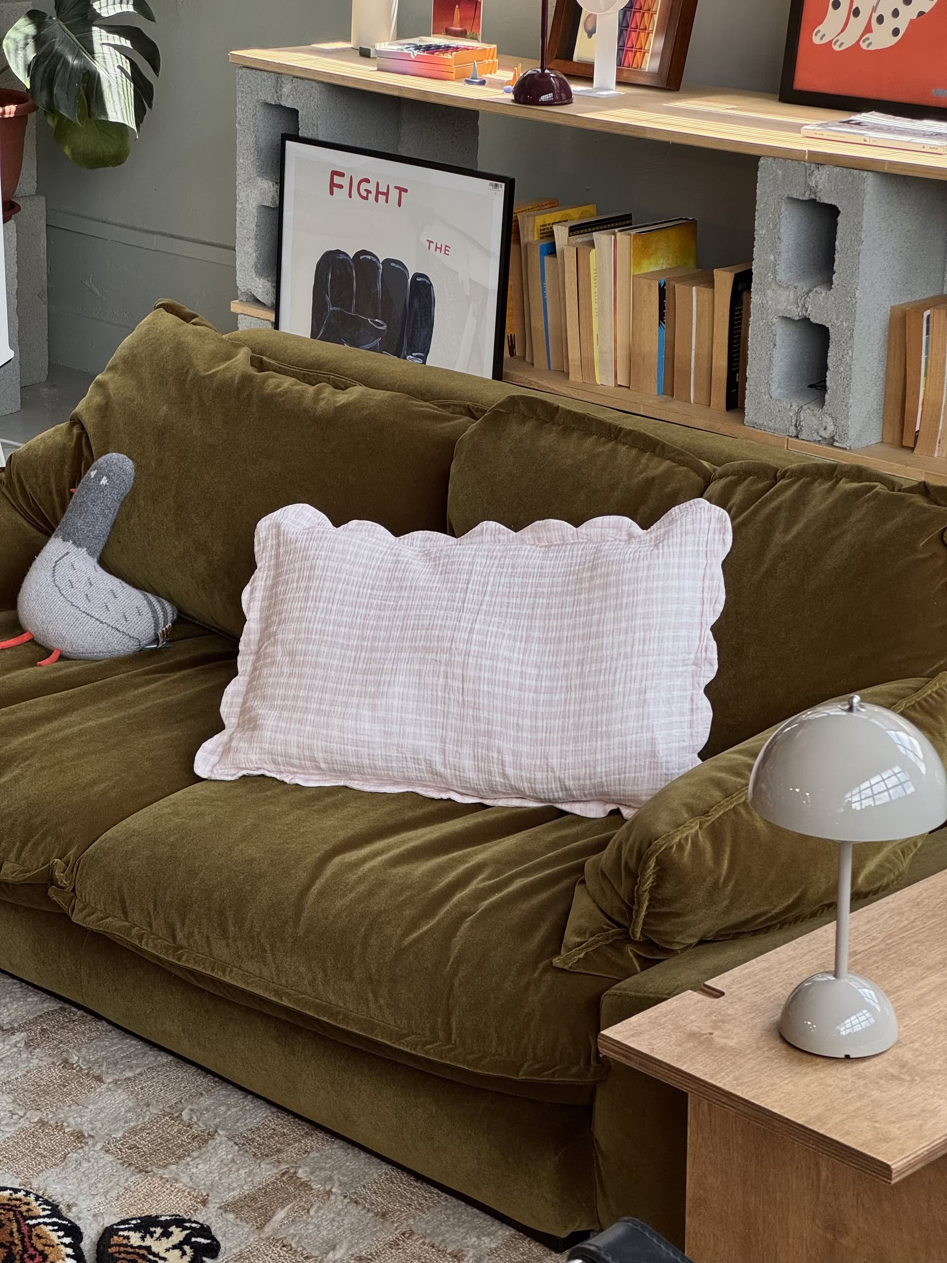 A cozy green velvet sofa features Soft Spot Soft Petal Cushion Covers Rectangle, Set of 2 (white), and a gray bird plush in the living room. Nearby are books, a lamp, and a framed “FIGHT” poster leaning against a shelf of books.