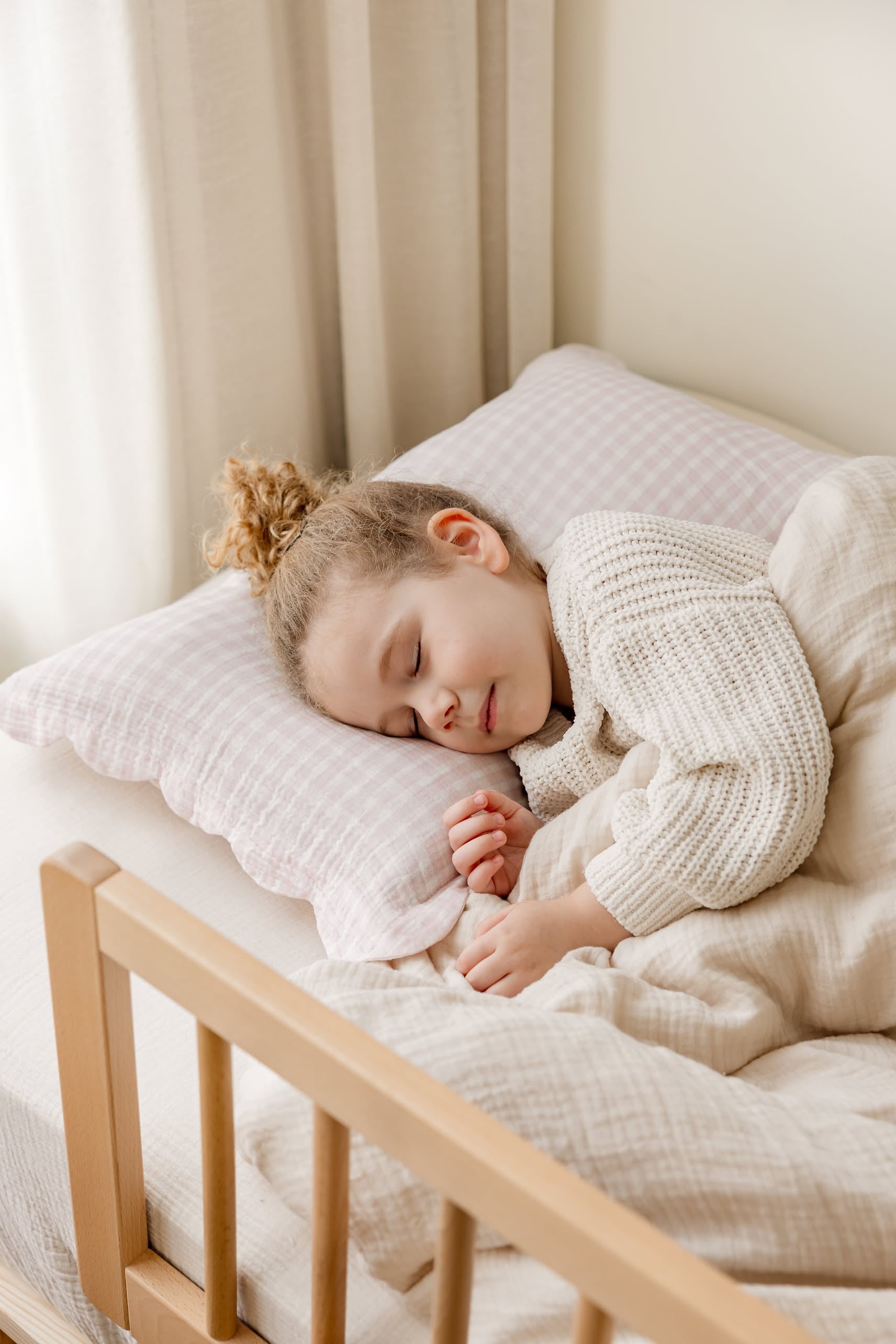 A young child with curly hair sleeps peacefully, cuddling a soft pillow wrapped in Soft Spot Soft Petal Cushion Covers Rectangle, Set of 2 by Soft Spot, and wearing a cozy sweater under a light blanket.