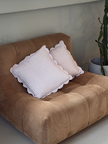 A plush brown corduroy sofa with two Soft Spot Soft Petal Cushion Covers by Soft Spot sits beside a large green cactus in a white planter against a light-colored wall.