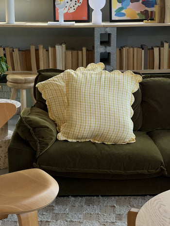 The Soft Spot Soft Petal Cushion Covers, Set of 2, from Soft Spot—one in yellow gingham and the other in colorful florals—decorate a beige couch, with neutral curtains in the background.