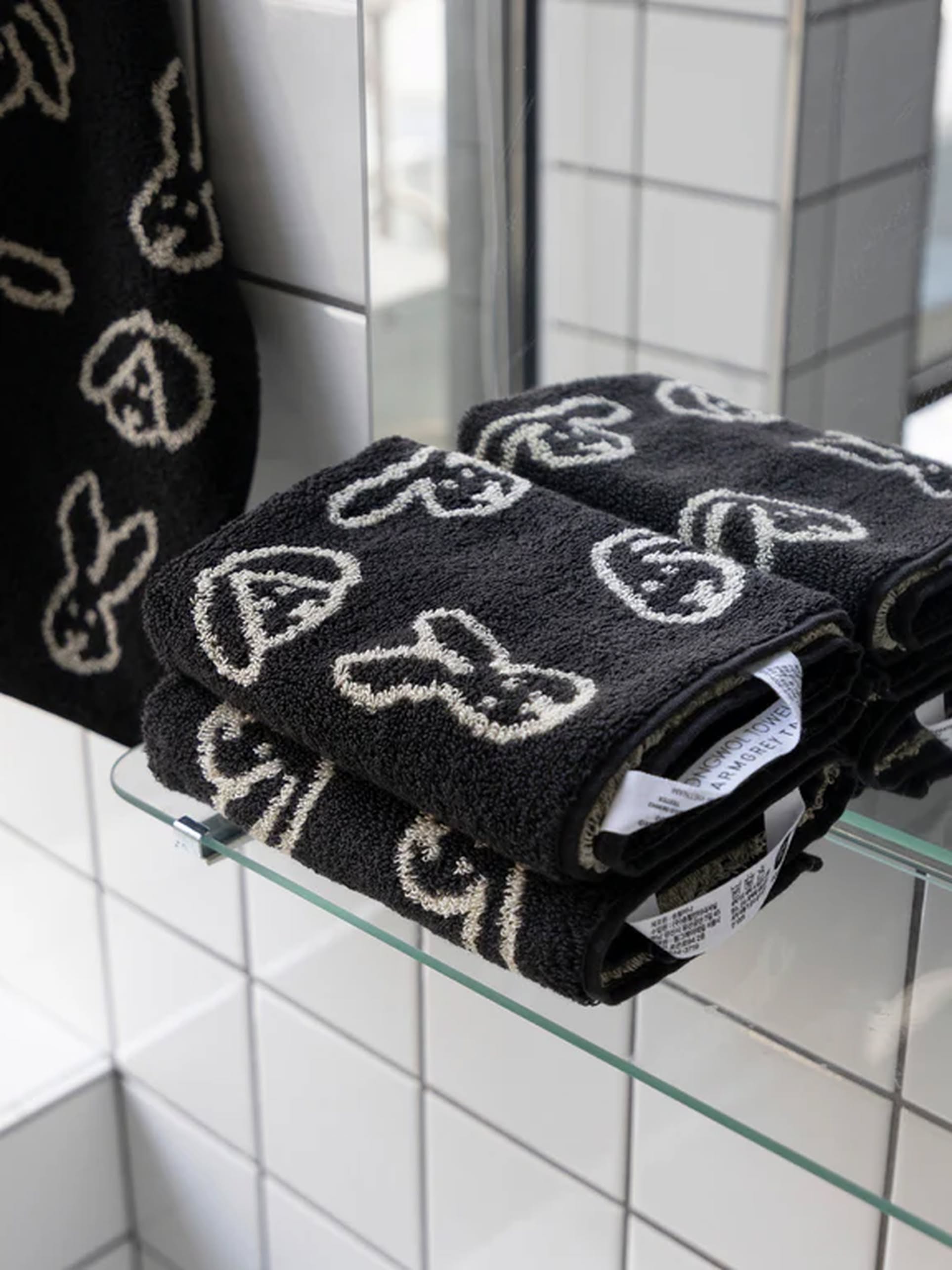 WARMGREY TAIL Bunny Bunny Hand Towels, featuring black soft cotton and white bunny face patterns, are neatly folded on a glass bathroom shelf, with a matching WARMGREY TAIL hand towel hanging nearby.